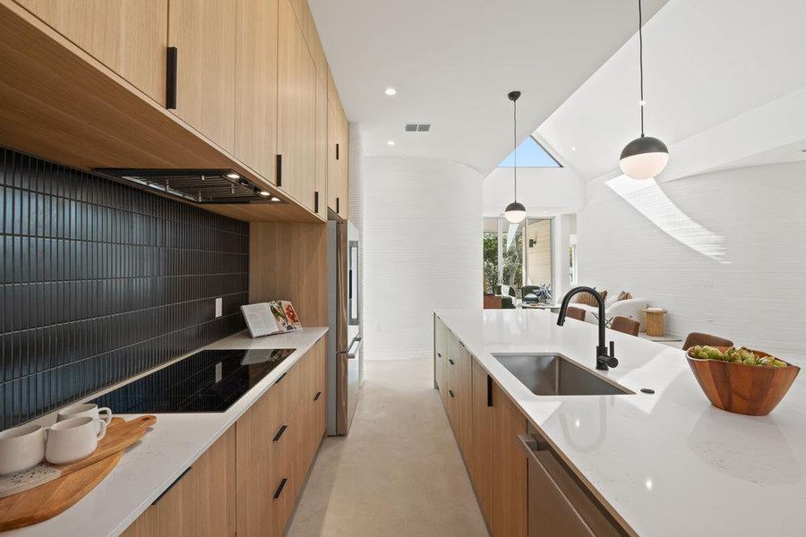Kitchen featuring modern cabinets, light stone countertops, vaulted ceiling, hanging light fixtures, and stainless steel appliances