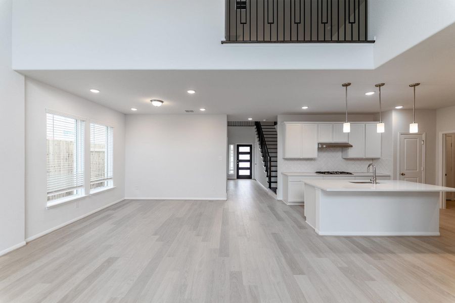 Kitchen featuring white cabinets, light wood-style flooring, hanging light fixtures, decorative backsplash, and open floor plan