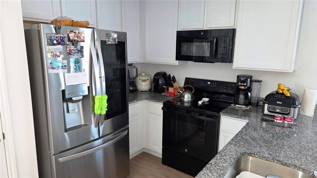 Modern kitchen featuring white cabinetry, granite-finish countertops, and wood-finish flooring