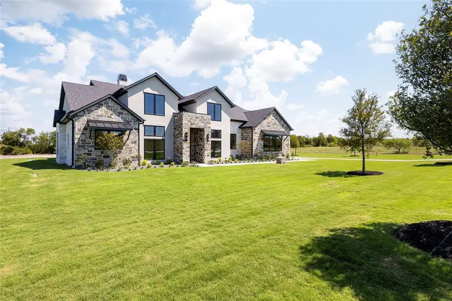 View of front facade with stone siding, stucco siding, and a front lawn