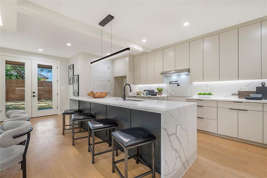 Kitchen with sink, pendant lighting, a kitchen island with sink, light wood-type flooring, and light stone countertops