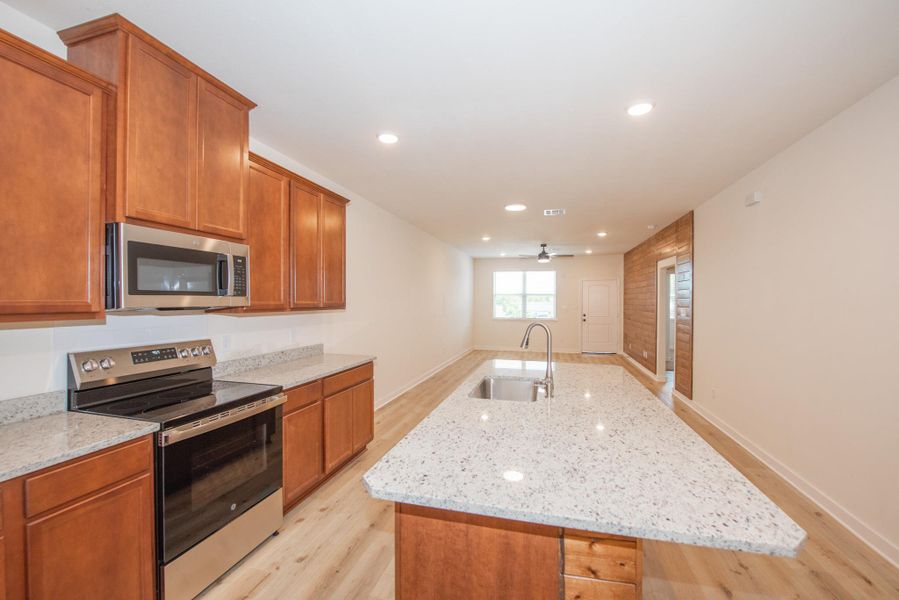 Kitchen with stainless steel appliances, an island with sink, recessed lighting, brown cabinetry, and light wood finished floors