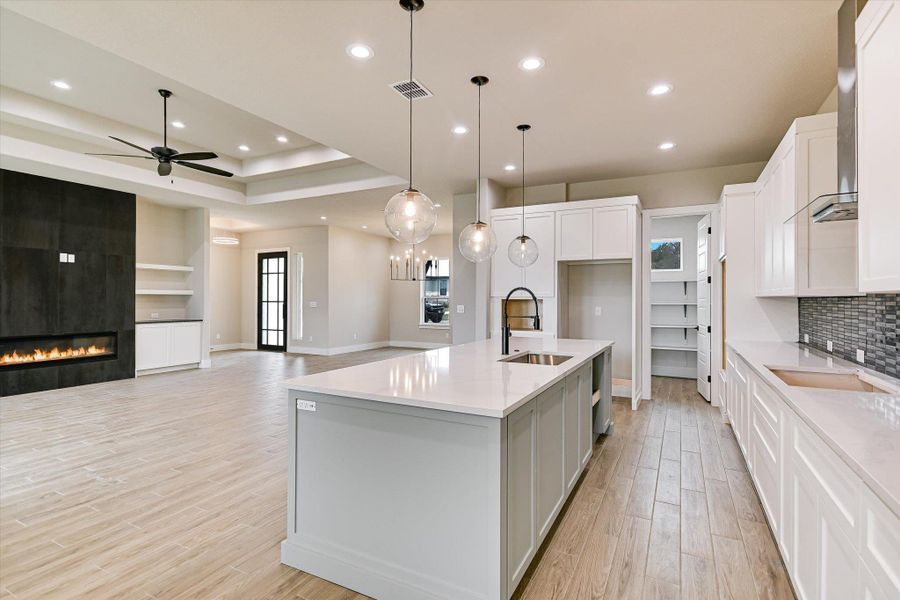 Kitchen featuring open floor plan, a center island with sink, white cabinets, a ceiling fan, and pendant lighting