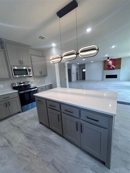 Kitchen with gray cabinets, range, decorative backsplash, light countertops, and open floor plan Kitchen with gray cabinets, range, decorative backsplash, light countertops, and open floor plan