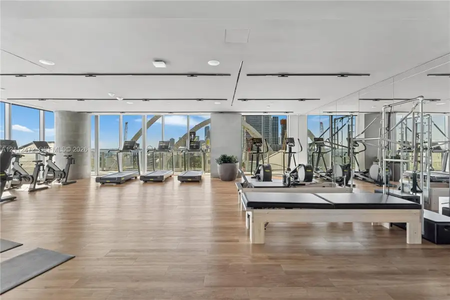 Fitness center featuring wood-finish flooring, floor-to-ceiling windows, mirrored walls, recessed track lighting, and a concrete structural column
