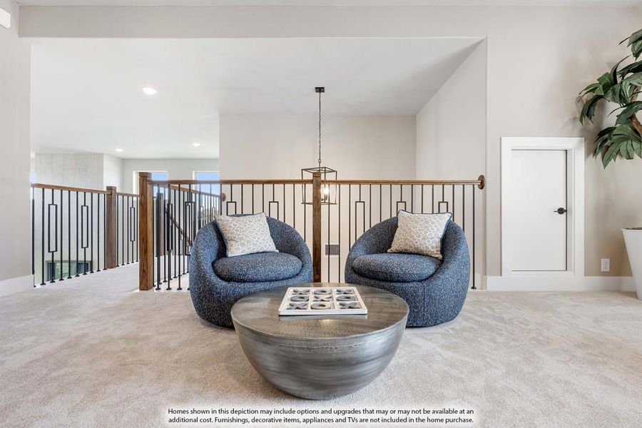 Upstairs loft seating area with two blue chairs, round coffee table, and metal railing overlooking staircase