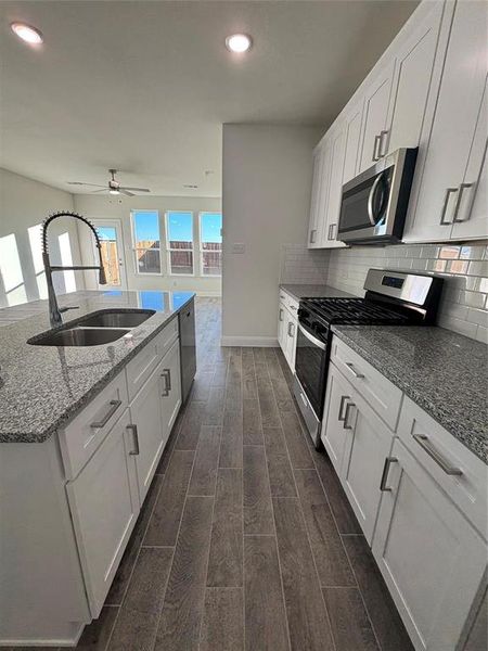 Kitchen featuring appliances with stainless steel finishes, a sink, wood finish floors, white cabinetry, and backsplash