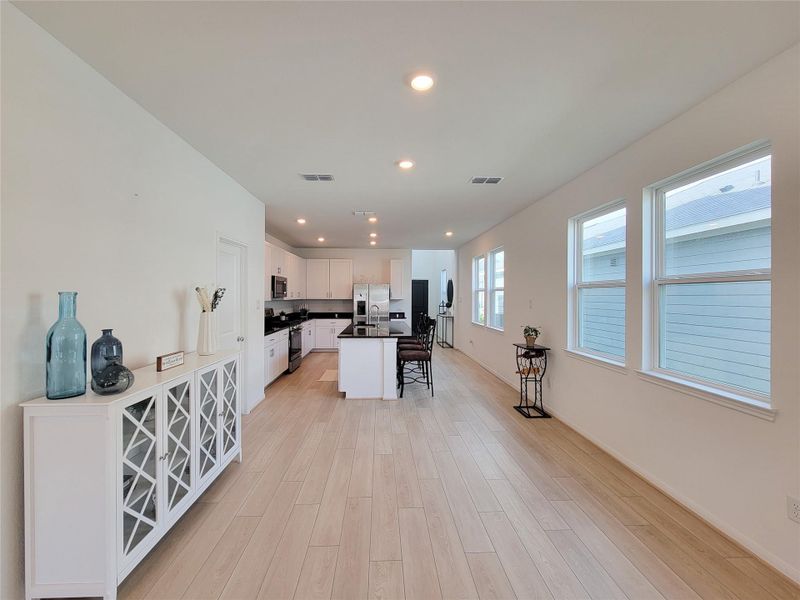 Spacious, open-concept kitchen and dining area with light wood flooring and abundant natural light. The kitchen features modern white cabinetry, stainless steel appliances, and a large island, creating a welcoming space for cooking and entertaining.