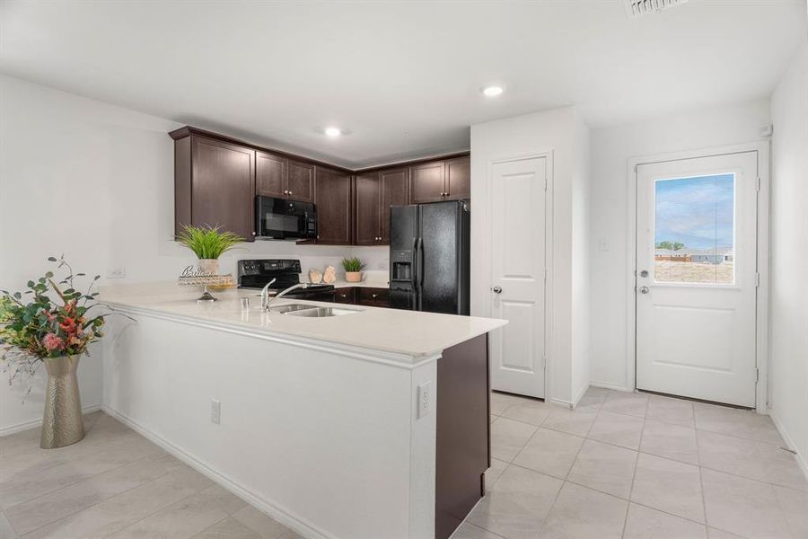 Kitchen with black appliances, light tile patterned floors, sink, dark brown cabinetry, and kitchen peninsula and pantry.