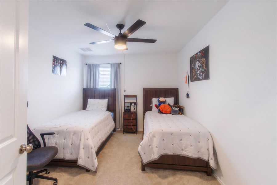 Spacious upstairs bedroom with carpeted floors and a ceiling fan, perfect for relaxing or accommodating guests.