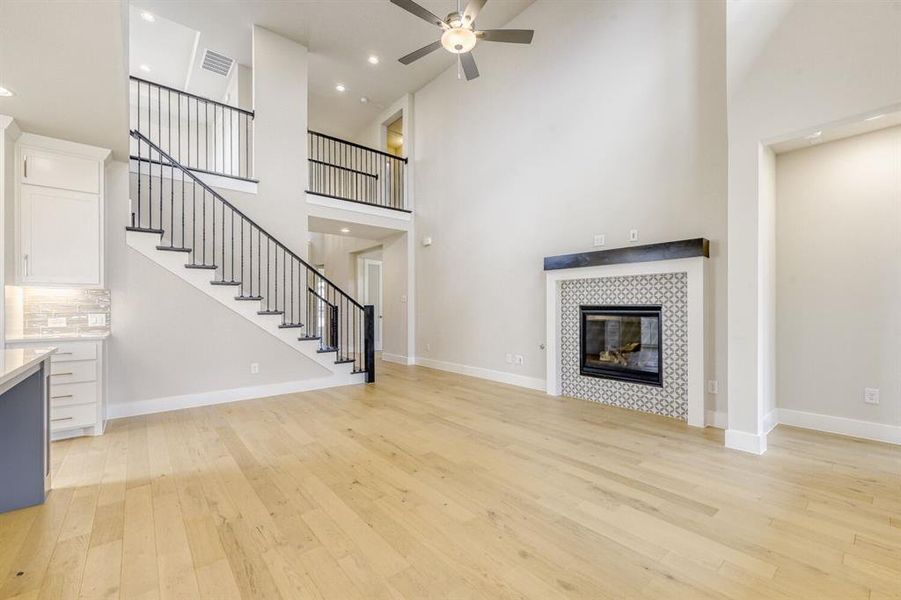 Unfurnished living room with ceiling fan, light wood-style floors, a tiled fireplace, and a high ceiling