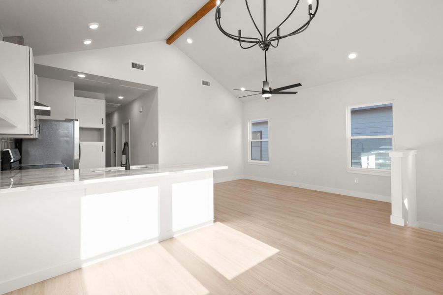 Kitchen featuring white cabinetry, a peninsula, light stone countertops, a chandelier, and light wood-style floors