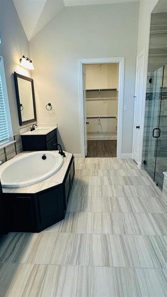 Full bath with a shower stall, vanity, a garden tub, lofted ceiling, and a walk in closet