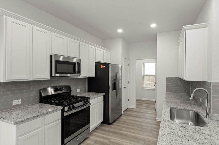 Kitchen with backsplash, appliances with stainless steel finishes, white cabinetry, light wood-type flooring, and recessed lighting Kitchen with backsplash, appliances with stainless steel finishes, white cabinetry, light wood-type flooring, and recessed lighting