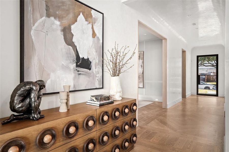 A grand first impression, this formal entryway is defined by its sophisticated design and impeccable craftsmanship. A striking steel-framed glass panel door welcomes natural light, complementing the elegant Venetian plastered walls and radius ceiling. The warmth of white oak hardwood floors, laid in a custom pattern, adds a refined touch to this beautifully curated space.