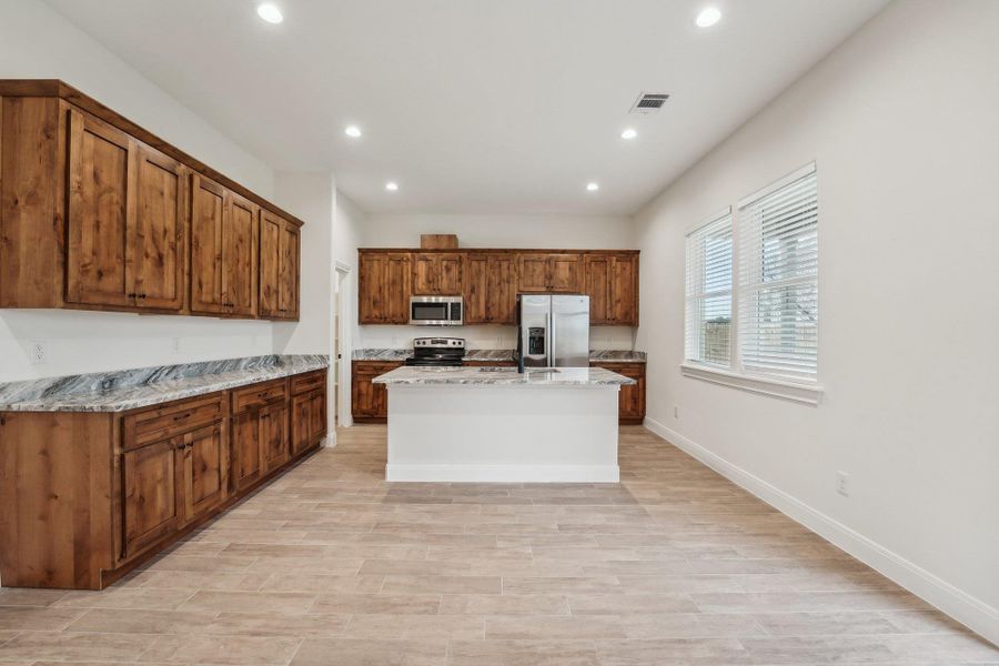 Kitchen with visible vents, baseboards, appliances with stainless steel finishes, brown cabinetry, and a kitchen island with sink Kitchen with visible vents, baseboards, appliances with stainless steel finishes, brown cabinetry, and a kitchen island with sink