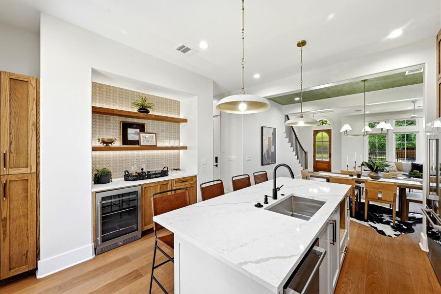 A well-appointed kitchen features a large island with sink, ample cabinetry, and a dedicated bar area with a wine cooler, connecting seamlessly to a dining space. A well-appointed kitchen features a large island with sink, ample cabinetry, and a dedicated bar area with a wine cooler, connecting seamlessly to a dining space.