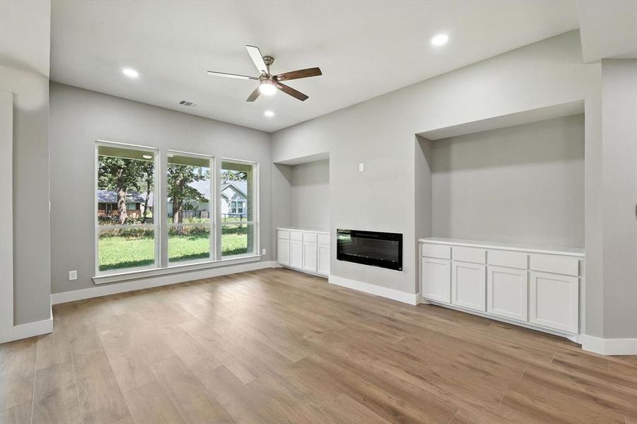 Unfurnished living room featuring a glass covered fireplace, light wood finished floors, a ceiling fan, and recessed lighting