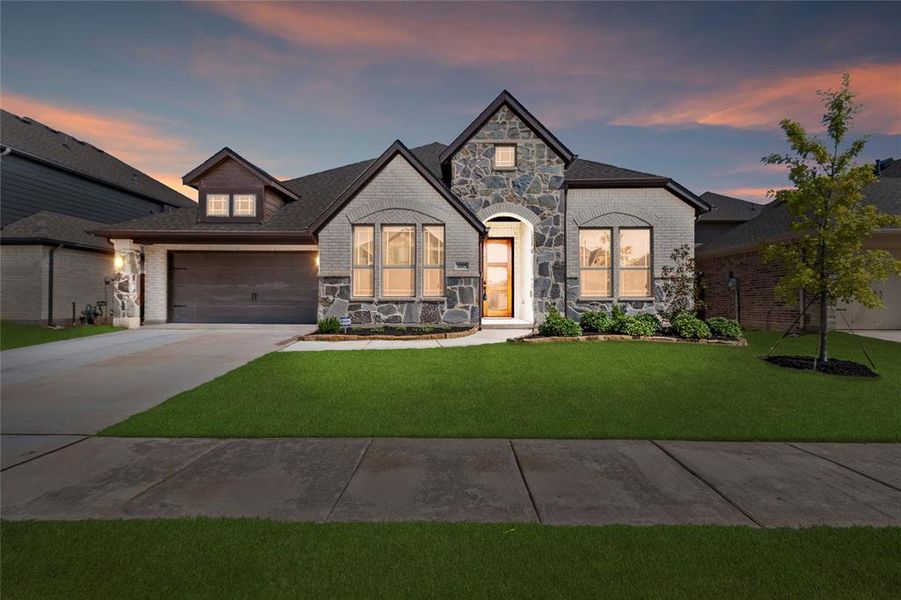 French country home with brick siding, stone siding, and concrete driveway