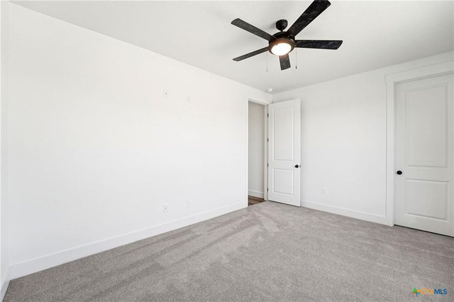 A well-lit bedroom featuring a ceiling fan and neutral carpeting, ready for personalization. A well-lit bedroom featuring a ceiling fan and neutral carpeting, ready for personalization.