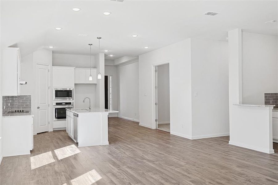 Kitchen with white cabinetry, sink, stainless steel appliances, light hardwood / wood-style floors, and a kitchen island with sink