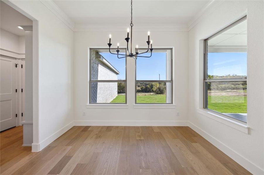 Unfurnished dining area with a notable chandelier, light hardwood / wood-style floors, and crown molding