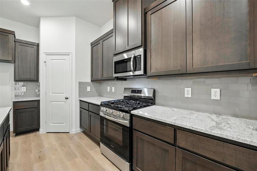 Kitchen with appliances with stainless steel finishes, light wood-style flooring, tasteful backsplash, and light stone counters