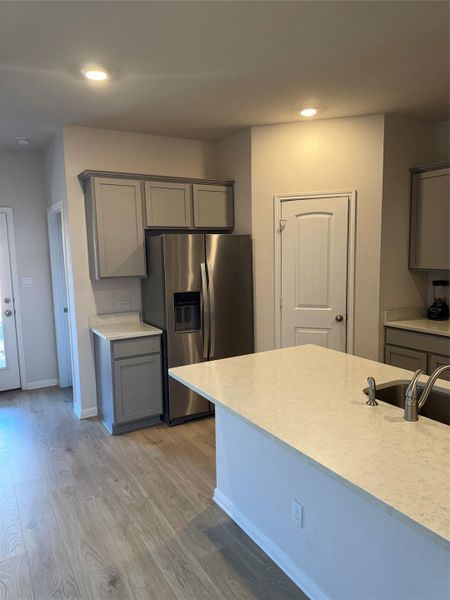 Kitchen featuring gray cabinetry, light countertops, stainless steel refrigerator with ice dispenser, light wood finished floors, and recessed lighting