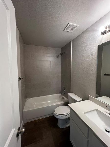 Full bathroom featuring tiled shower / bath, a textured ceiling, toilet, vanity, and hardwood / wood-style flooring