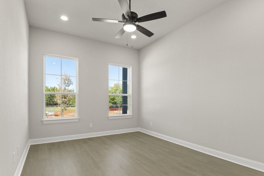 Image of two story home upstairs bedroom with light brown wooden flooring and light grey painted walls with two windows and a ceiling fan