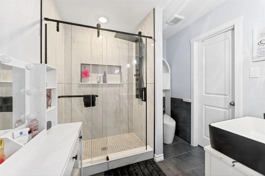 Modern bathroom featuring a glass-enclosed shower with black-framed sliding door, light-toned vertical wall tiles, and a hexagonal mosaic floor