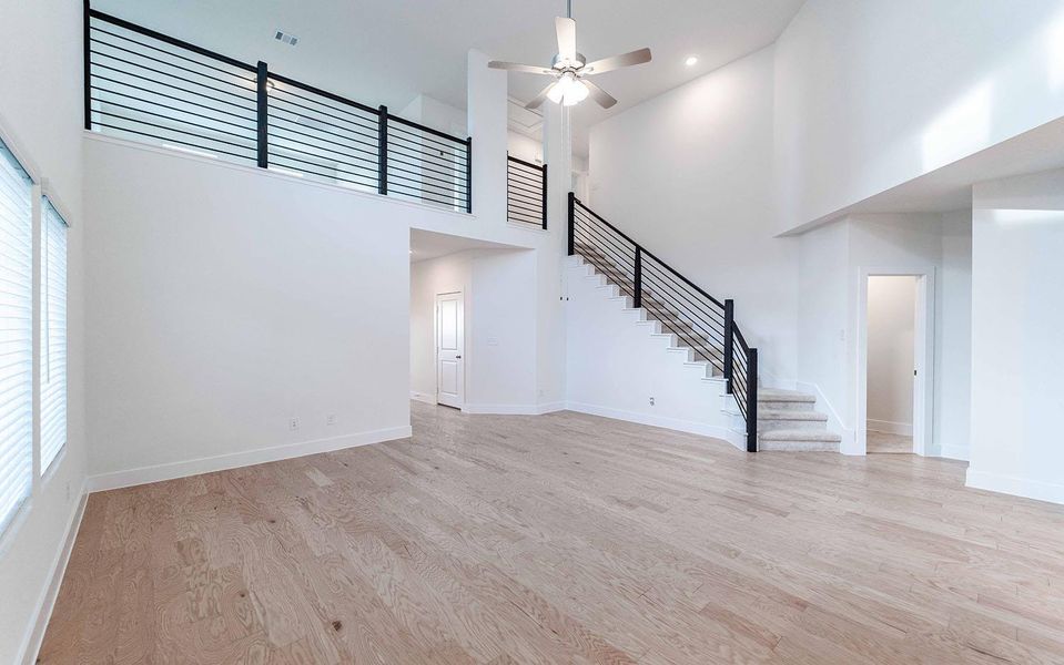 Unfurnished living room featuring a high ceiling, light wood-type flooring, and a ceiling fan Unfurnished living room featuring a high ceiling, light wood-type flooring, and a ceiling fan