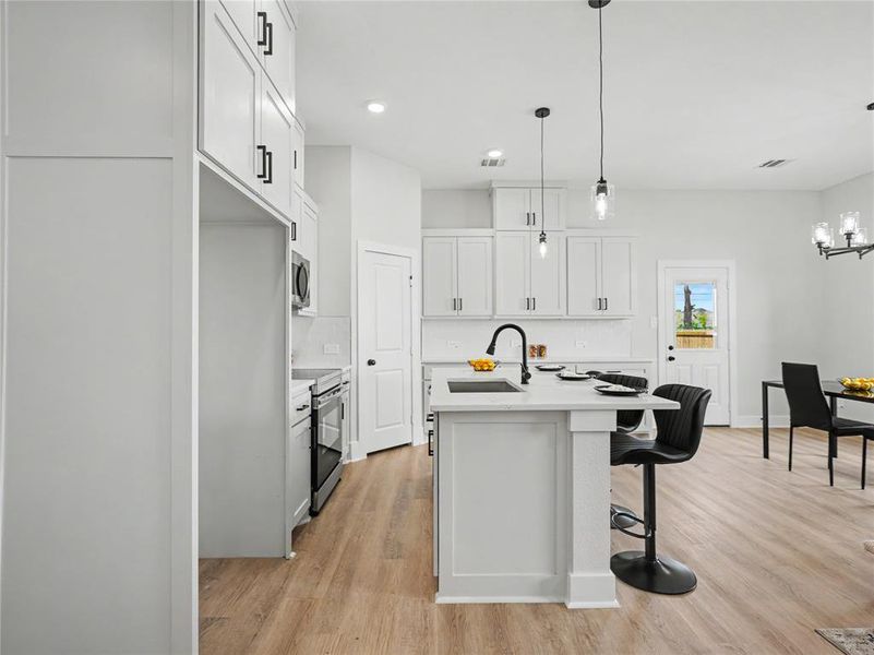 Modern kitchen featuring white cabinetry with matte black hardware, stainless steel appliances, a center island with seating, and wood-finish flooring Modern kitchen featuring white cabinetry with matte black hardware, stainless steel appliances, a center island with seating, and wood-finish flooring
