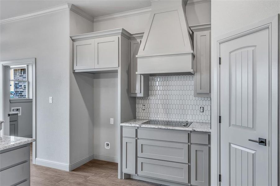 Kitchen featuring light stone counters, light hardwood / wood-style floors, black electric cooktop, crown molding, and premium range hood