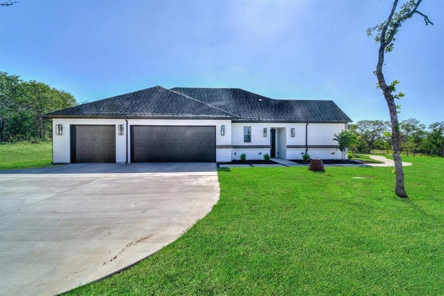 View of front of house with concrete driveway, an attached garage, a front lawn, and a shingled roof