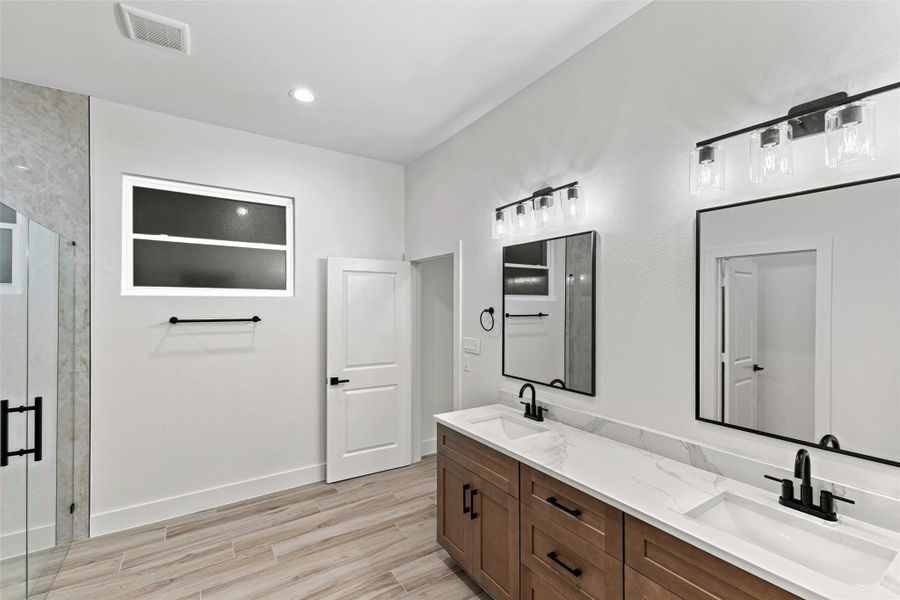 This modern bathroom features a dual-sink vanity with a quartz countertop, sleek black fixtures, and ample lighting. This modern bathroom features a dual-sink vanity with a quartz countertop, sleek black fixtures, and ample lighting.