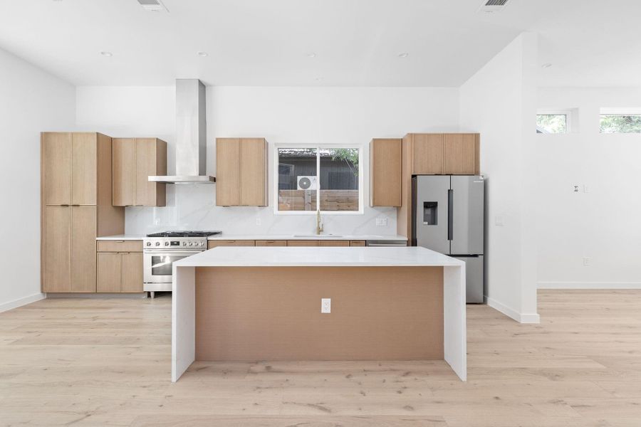 Kitchen with a center island, light countertops, light wood finished floors, and appliances with stainless steel finishes Kitchen with a center island, light countertops, light wood finished floors, and appliances with stainless steel finishes