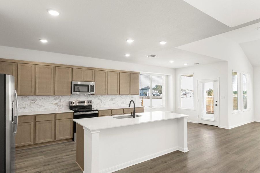 Kitchen with appliances with stainless steel finishes, a center island with sink, light stone counters, dark wood-style flooring, and decorative backsplash