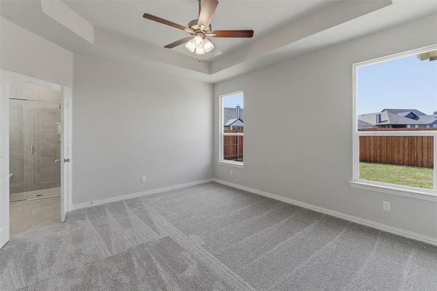 Unfurnished bedroom with a raised ceiling, light colored carpet, ceiling fan, and ensuite bath