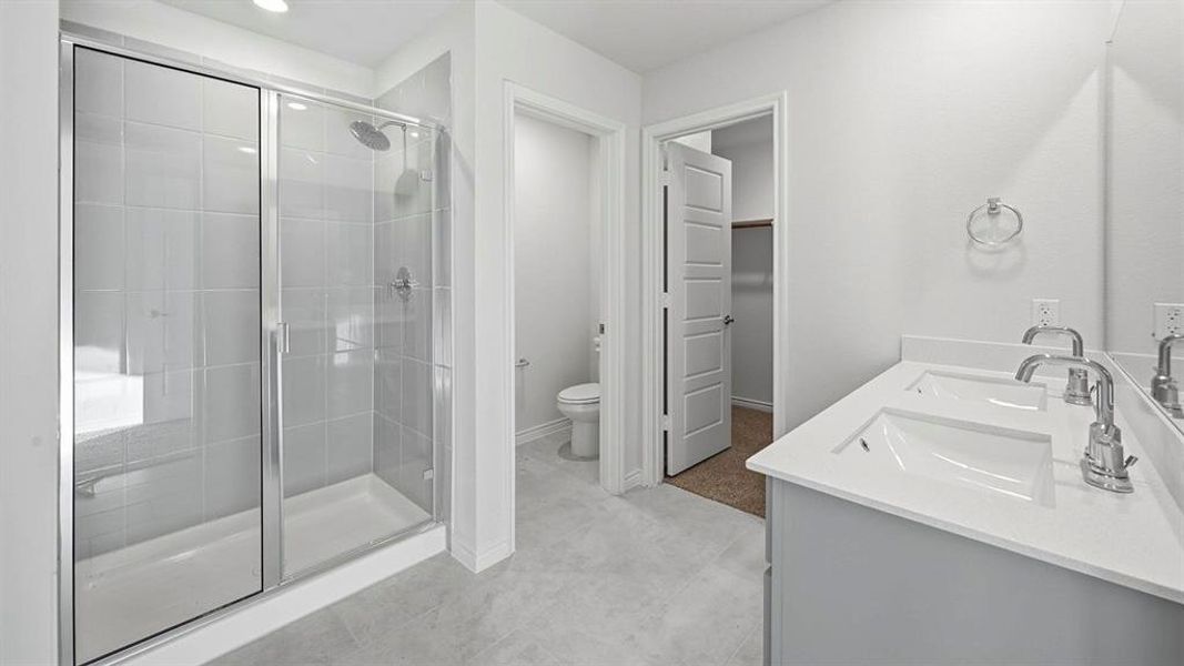 Bathroom featuring a double vanity with white countertops, a walk-in shower with a glass enclosure, and light-colored tile flooring