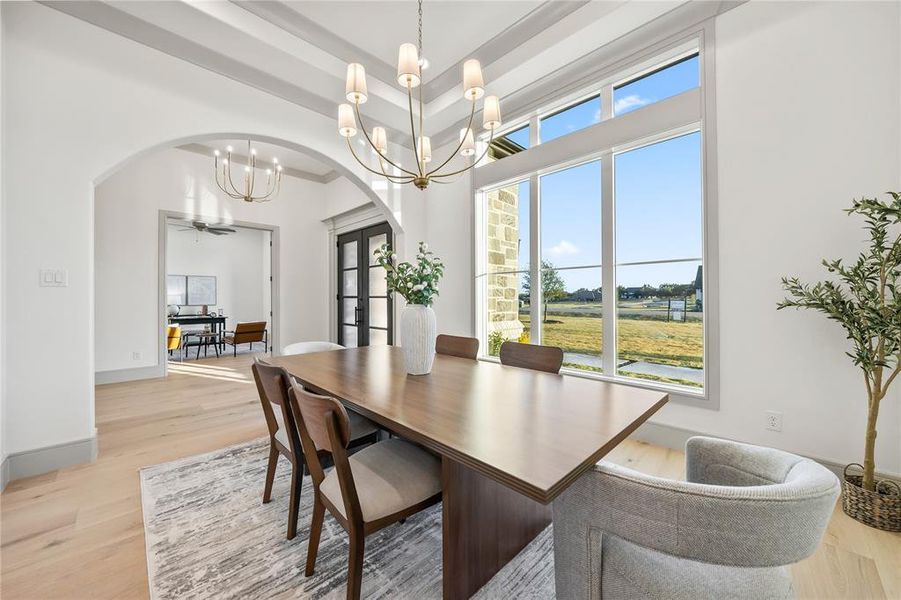 Dining area featuring a coffered ceiling, large picture windows, light wood-finish flooring, and an arched entryway