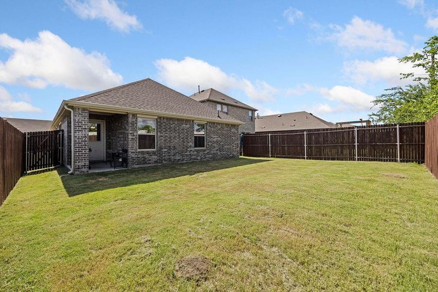 Expansive backyard featuring a manicured lawn, full privacy fencing, and a covered concrete patio Expansive backyard featuring a manicured lawn, full privacy fencing, and a covered concrete patio