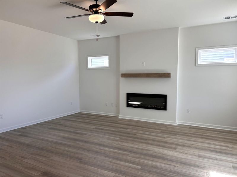 Unfurnished living room featuring a glass covered fireplace, wood finished floors, and ceiling fan