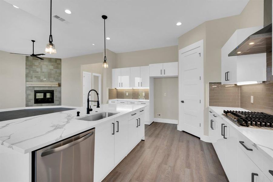 Kitchen with appliances with stainless steel finishes, a multi sided fireplace, sink, white cabinetry, and light hardwood / wood-style floors