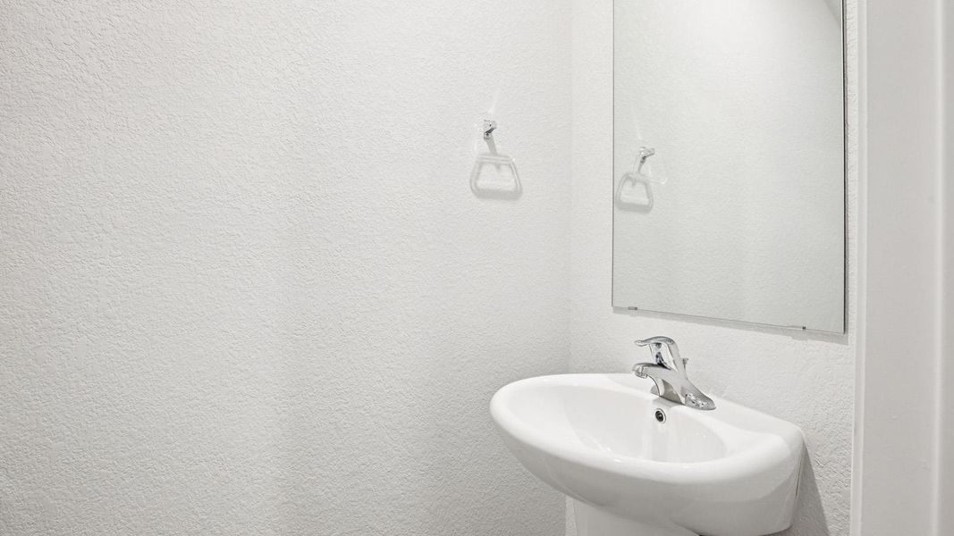 Wall-mounted pedestal sink with polished chrome faucet and frameless wall mirror