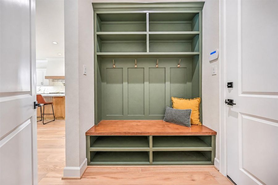 Thoughtful details continue with a custom drop zone featuring a built-in bench, open shoe storage, upper cubbies, hooks and a rich accent finish — a functional landing spot tucked just off the kitchen.