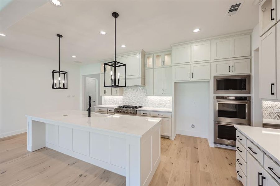 Kitchen with backsplash, stainless steel appliances, light hardwood / wood-style floors, and a kitchen island with sink