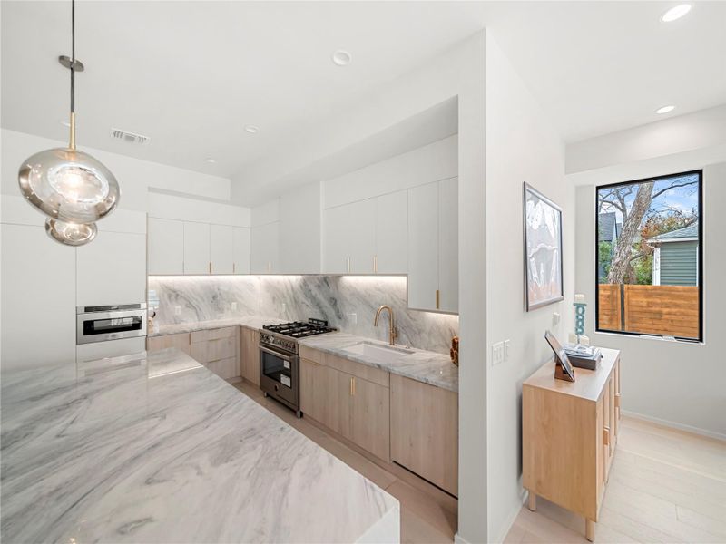 Dual tone kitchen featuring modern cabinets, light stone counters, tasteful backsplash, high end range, and hanging light fixtures