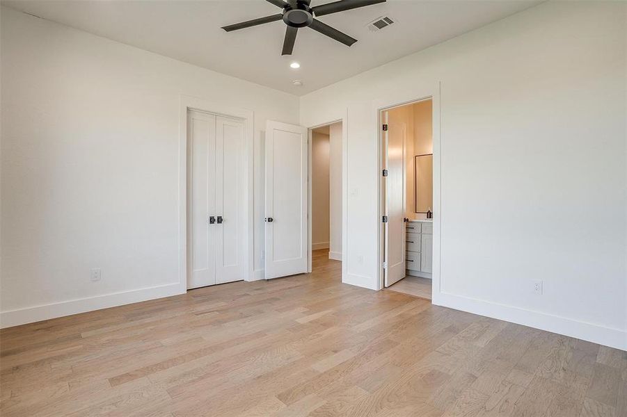 Unfurnished bedroom featuring a closet, ensuite bathroom, light wood-type flooring, and ceiling fan