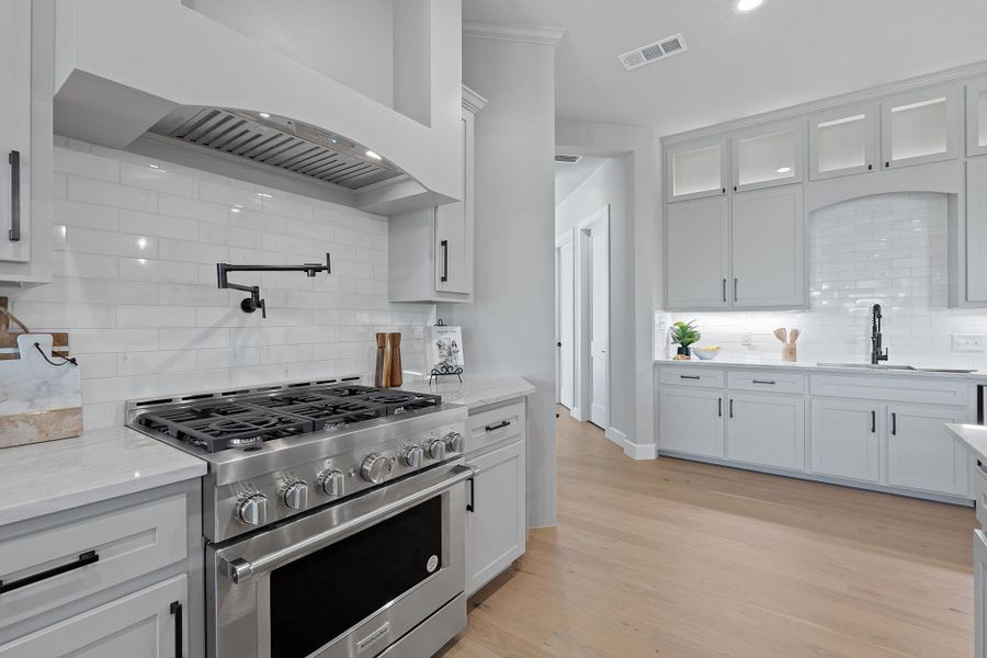 Kitchen featuring high end stainless steel range, backsplash, custom exhaust hood, white cabinetry, and recessed lighting